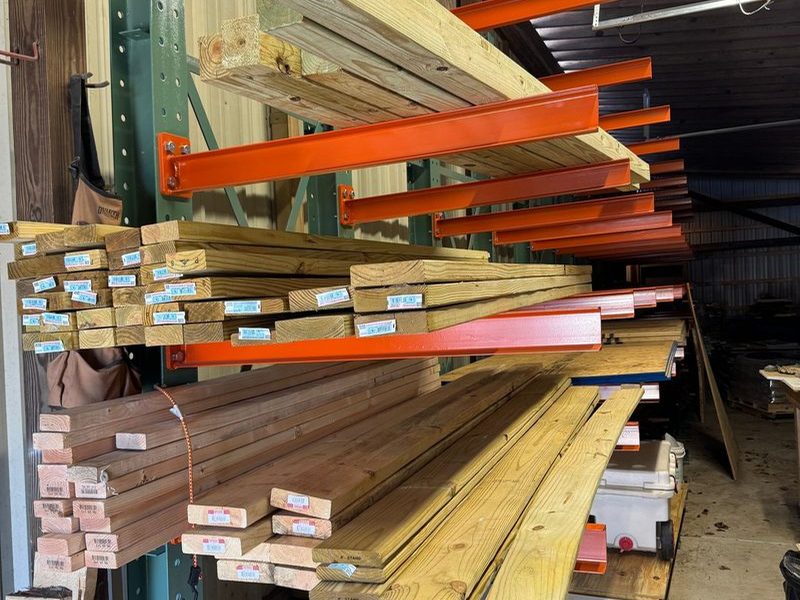 An orange-armed cantilever rack loaded with pressure-treated and framing lumber in a covered shed
